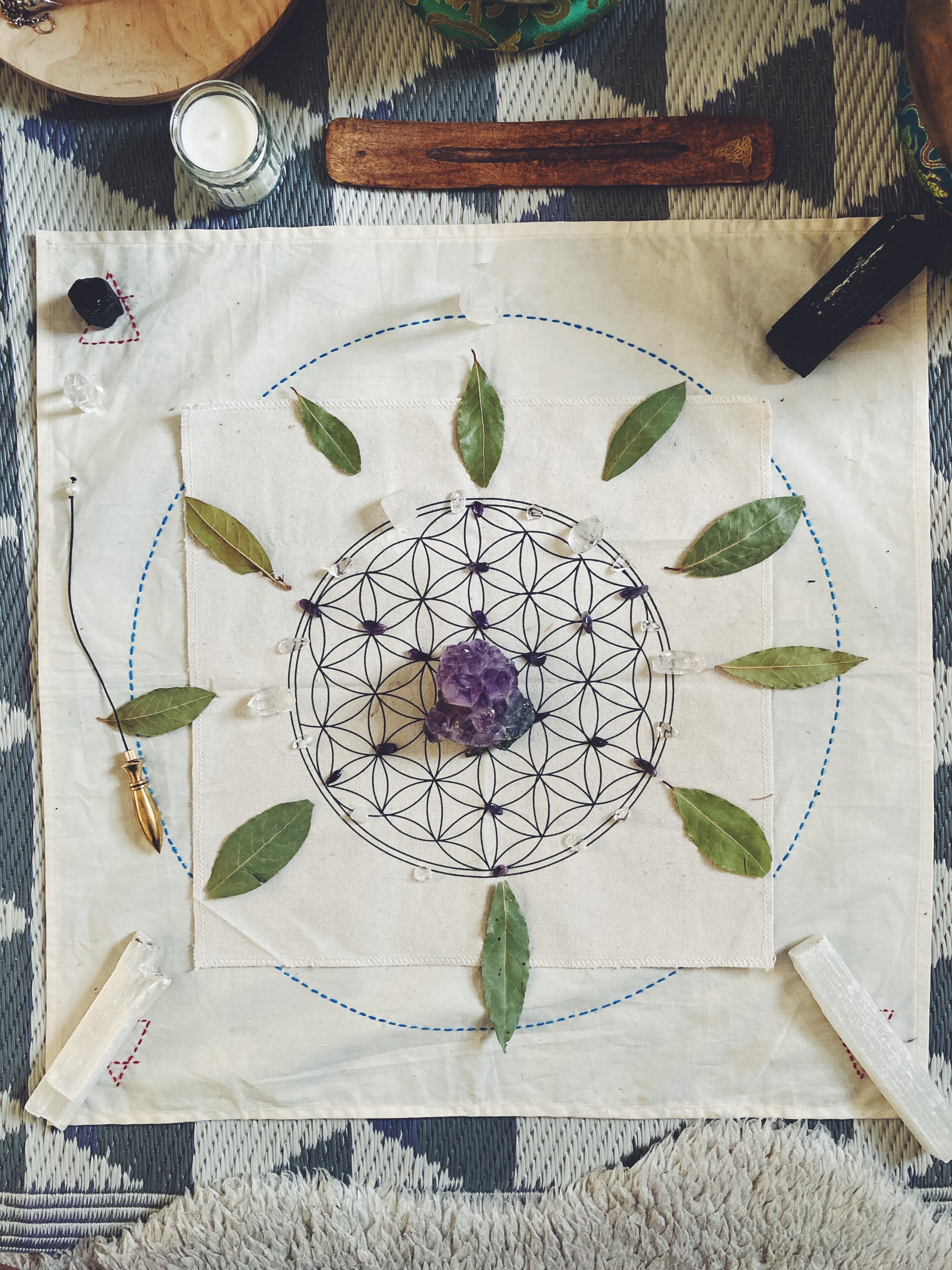 A flower-of-life cloth arranged with leaves, crystals and white selenite pieces.