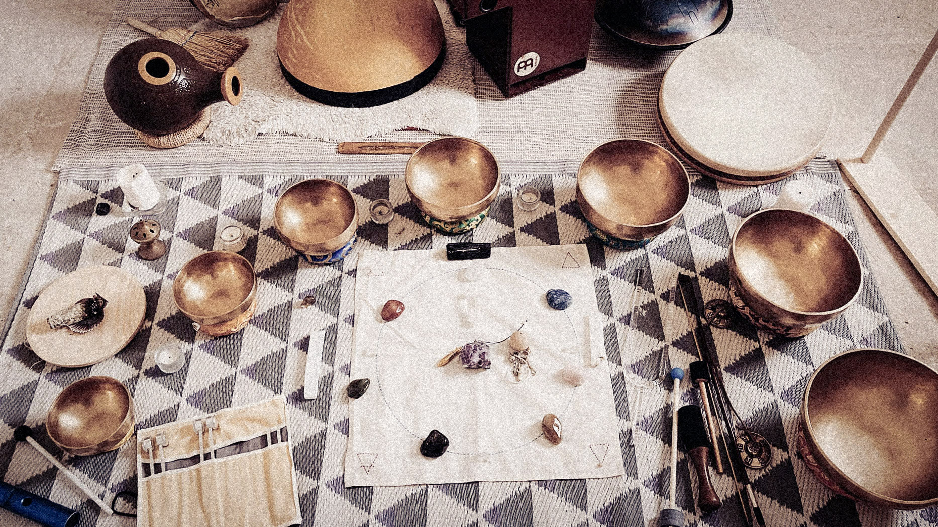 An overhead arrangement of bowls, tuning forks and resonant objects on woven cloth.